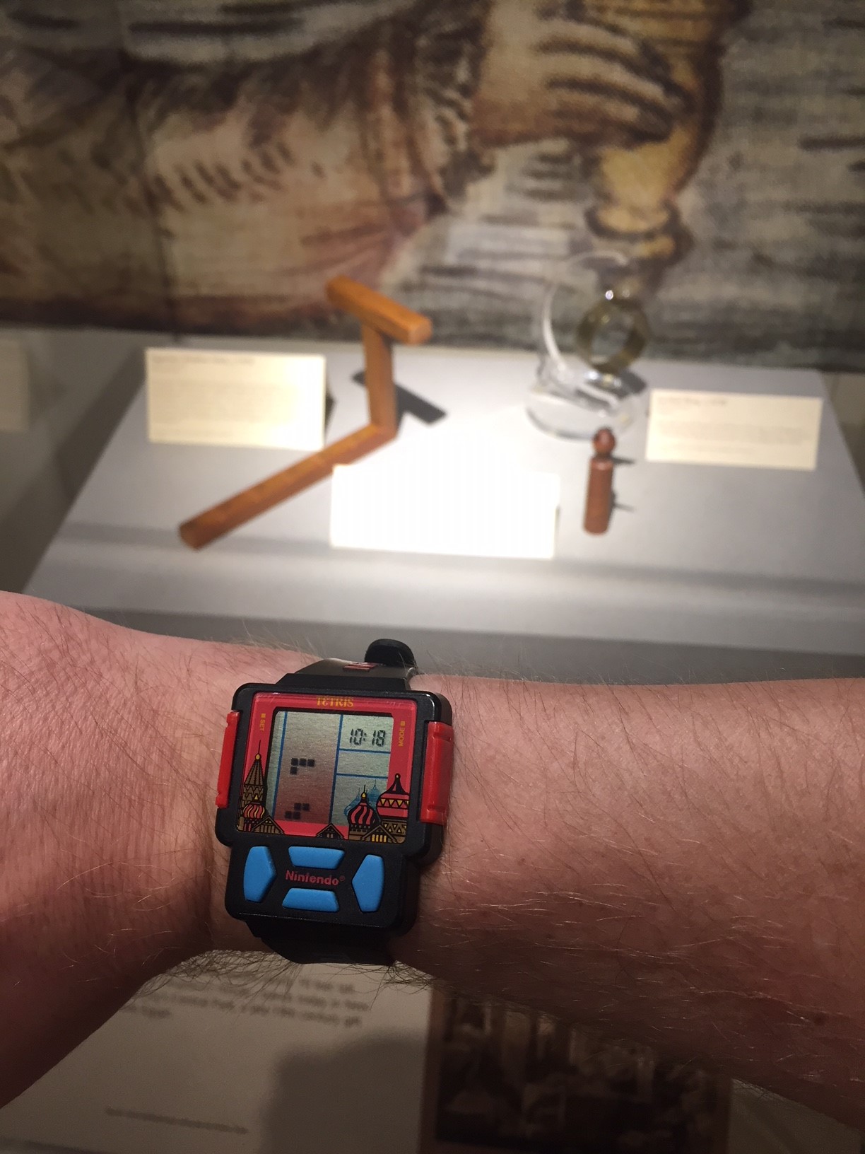 Tetris watch on man's wrist with shadow clocks in background at a museum
