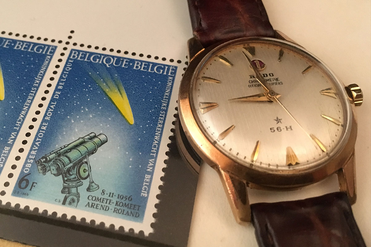 vintage Rado wristwatch beside a postage stamp depicting a telescope viewing a comet flying in a night sky