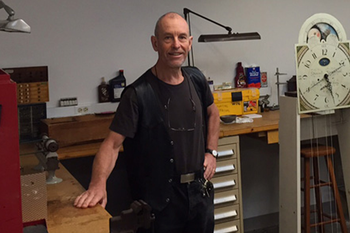 Adam Harris poses in front of various horological workbenches and  equipment